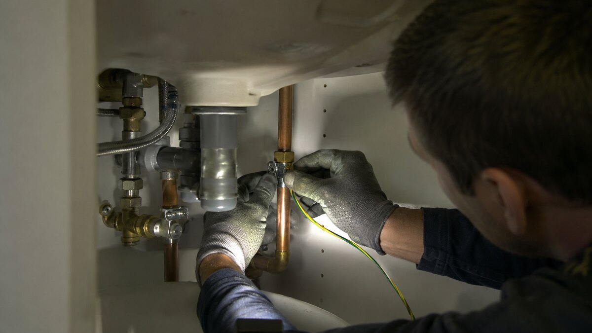Elektricien sluit een aardingskabel aan onder een wastafel in Antwerpen